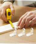 Man measuring wooden board with tape, showcasing 10 pcs clear acrylic corner brackets for furniture reinforcement, L shaped braces.