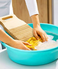 No Sweat Bamboo Washboard For Hand Washing Clothes With Non Slip Base and Deep Grooves being used in a blue basin.