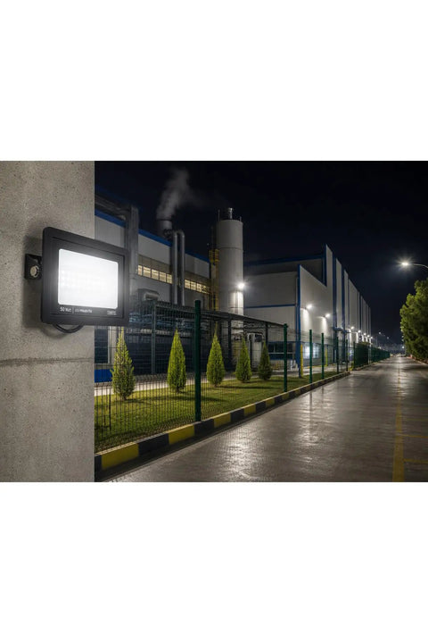 SODEF 50W LED Floodlight White Light IP65 Water-Resistant Outdoor High Lumen Energy Saving on a concrete wall illuminating a factory.