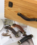 Leather Suitcase Luggage Pull Handles 2 Piece Set, black brown finish, on wooden cabinet with attached hardware, for doors and drawers