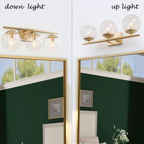 Three Light Gold Vanity Light Fixture With Clear Globe Glass Shades And Slim Taper Arm For Modern Bathroom Decor reflecting in mirror