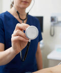 Front view of stethoscope diaphragm replacement with silver disk held by clinician in blue scrubs