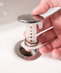 Hand holding The Real Deal Drain Protector And Hair Catcher Combo For Bathtubs And Sinks Chrome Finish with hair caught.