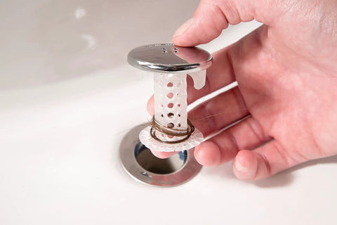 Hand holding The Real Deal Drain Protector And Hair Catcher Combo For Bathtubs And Sinks Chrome Finish with hair caught.