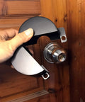 Hand holding a black Door Knob Lock Cover No Drill Quick Install Outside Locking Shield For Privacy And Keyhole Safety, prevents turning.