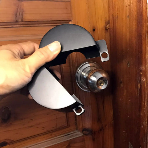 Hand holding a black Door Knob Lock Cover No Drill Quick Install Outside Locking Shield For Privacy And Keyhole Safety, prevents turning.