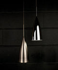 Two Dope Bullet LED Pendant Fixtures With Canopy In Chrome, sleek design, dimly lit against a dark brick wall backdrop.