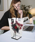 Plastic Bouquet Bags With Handles For Flower Packaging holding roses, displayed on a desk next to a woman using a laptop.