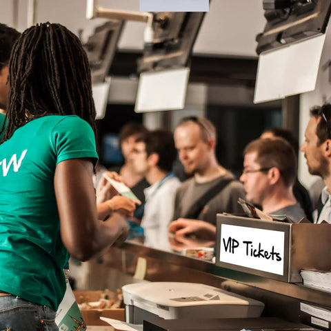 People purchasing VIP tickets at a busy counter, staff assisting customers in green shirts.