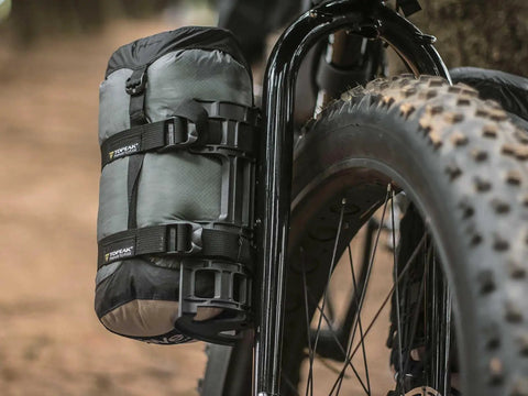VersaCage Adventure Cage With Adjustable Mounting System And VersaMount Clamps And Straps holding a dry bag on a bike fork