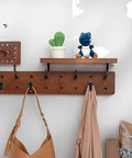 Wall-mounted wooden coat rack with hooks, hanging bags and jackets, cactus plant, and clock on the shelf.