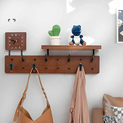 Wall-mounted wooden coat rack with hooks, hanging bags and jackets, cactus plant, and clock on the shelf.