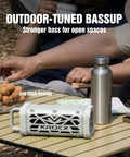 Rugged Aluminum Bluetooth Speaker With 45W Power Deep Bass IP68 Waterproof Magnetic Mounting TWS Pairing Long Battery Life Go To Outdoor Speaker For Golf Carts Camping And Beach Adventures In A Cloud Dancer Metallic Finish sits on a picnic table with water bottles and snacks.