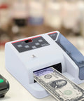 Money Counter Machine With UV MG WM Counterfeit Detection on table with bill being counted, compact design, LED display visible.