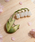 Delicate Lily Of The Valley Brooch For Women Featuring Tiny Bell Shaped Petals Lightweight Floral Pin on wooden surface.