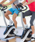 Two people riding stationary bikes indoors with 2 Pairs Universal Exercise Bike Pedal Straps For Home Gym Durable Rubber Straps Built Wider