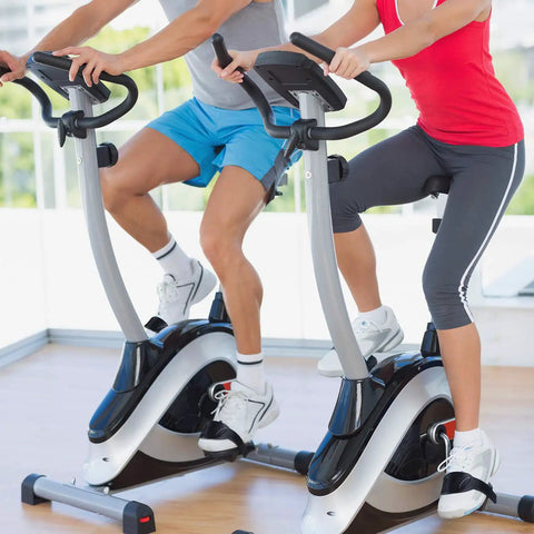 Two people riding stationary bikes indoors with 2 Pairs Universal Exercise Bike Pedal Straps For Home Gym Durable Rubber Straps Built Wider