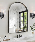 Winsmart Black Wall Sconces Set of Two Hard Wired with Clear Glass Shade beside a large arched mirror in a bathroom.