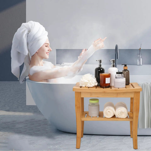 19 Inch Bamboo Shower Bench With Storage Shelf next to a bathtub with toiletries and towels on its two-tier wooden spa seat.
