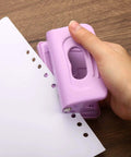 Hand using 2 Hole Paper Punch One Quarter Inch Pink Metal Hole Puncher, handles up to 8 sheets, on white paper, desk office gadget