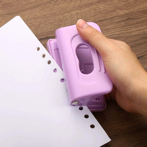 Hand using 2 Hole Paper Punch One Quarter Inch Pink Metal Hole Puncher, handles up to 8 sheets, on white paper, desk office gadget