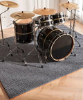 Pro Grade Soundproof Acoustic Pads Thick Non Slip Rubber Mat For Drum Kits And Home Studios under a black drum set on a textured floor.