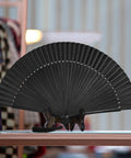 Black Hand Fan For Stage And Rave Dancers With Elaborate Design And Satisfying Snap Clack Go To Handheld Fan For Line Dancers 13 Inch Closed Size For A Bold Onstage Statement displayed open on a table.