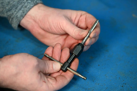 Hands holding T Handle Tap Wrench 1/4 Inch For Easy Tap Install And Precise Threading No Frills Pro Grade Tool in workshop setting.