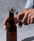 Close-up of a metal bottle opener with a circular ring used to open a brown glass beer bottle