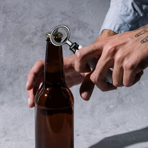Close-up of a metal bottle opener with a circular ring used to open a brown glass beer bottle