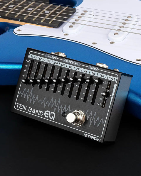 10 Band EQ Pedal for Electric Guitar and Bass With 31.25 Hz to 16 KHz Range, Each Band Delivers Up to 12 dB Gain or Cut, Durable Aluminum Alloy Build, Easy Stage and Studio Tone Shaping for Electric Players on black surface next to blue electric guitar.
