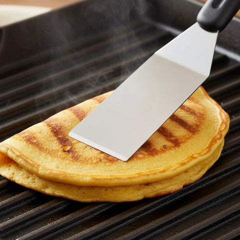Mini stainless steel spatula flipping a pancake on a grill.