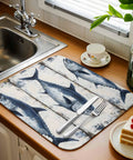 Blue Tuna Oil Painting Dish Drying Mat 18 X 24 Inches on wooden counter next to sink with cutlery and slice of cake.