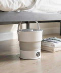 Compact Folding Mini Washing Machine Portable Laundry Basin Road Trip Ready Dorm Staple under bed with folded clothes nearby.