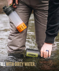 Person using GeoPress 24 Oz Water Purifier Bottle For Hiking And Camping, Easy Fill Press Drink System in a river