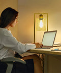 Industrial Table Lamp Set Of 2 With Gold Finish, clear glass shade emitting warm light on desk, woman working on laptop nearby