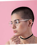 Person wearing glasses with pink frames and buzz-cut hairstyle against a pink background.