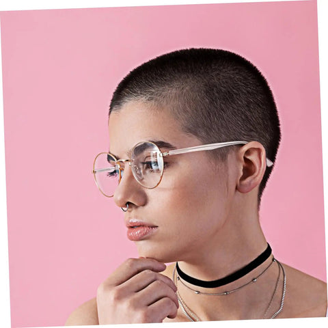 Person wearing glasses with pink frames and buzz-cut hairstyle against a pink background.