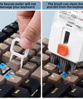 All In One Keyboard Cleaning Kit For Laptops And PCs With Retractable Brush Soft Cloths Keycap Puller Lens Pen Flocking Sponge And More The Ultimate Electronic Cleaner Kit For iPhone iPad MacBook Earbuds Cameras Monitors Patented Design showing keycap puller and brush in use on a keyboard.