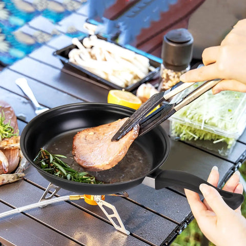 Cooking steak in Travel Ready 13 Piece Nonstick Cookware Set with lightweight cast iron pan and nylon tongs on campsite table