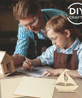 Front view: DIY Crafts basswood craft sheets on table with wooden house and sailboat; adult and child wearing safety goggles