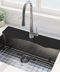 Extended Silicone Faucet Splash Guard And Sink Overflow Mat With Integrated Sponge Rest And Rapid Drain Cutouts To Keep Your Kitchen Counter No Sweat And Always Looking Sharp In Rich Matte Black positioned above a stainless steel sink.