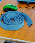 Blue insulated water bladder tube cover on a wooden table with green mouse; keeps hydration cold or hot, 92cm length.
