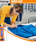 Woman using Permanent Fabric Glue 60 ML Washable Clear Clothing Glue For Rhinestones Patches Clothes Denim Leather Polyester Fabrics And Doll Repair Quick Strong Hold No Sew Without Needle And Thread on blue fabric