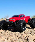 Red Volcano One Sixteenth Scale RC Monster Truck With Four Wheel Drive on rocky terrain, showcasing its large tires and rugged design.