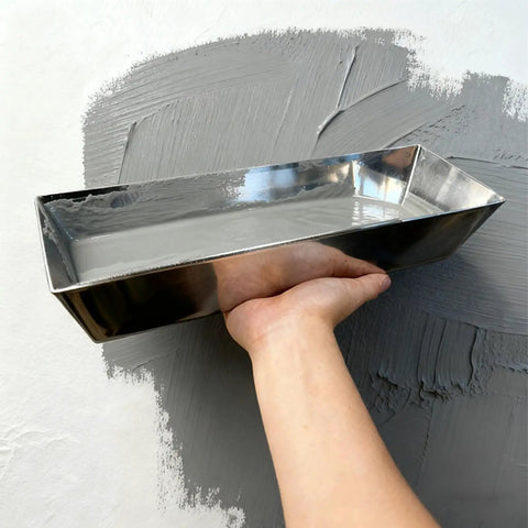 Hand holding shiny metal mudding tray filled with wall joint compound, used for wall and ceiling repairs in Kick Ass 11 Piece Drywall Tool Set With Telescopic Extension Pole And Paint Roller For Wall And Ceiling Mudding Taping Smooth Repairs And Home Renovation Work.