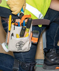 Worker wearing canvas and leather 5-pocket tool pouch with chain tape thong and tunnel belt connection, beige, fits up to 2¼ inches.