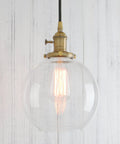 Dope Industrial Brass Pendant Light With 7.9 Inch Clear Glass Shade hanging against white wall, warm gold finish visible.