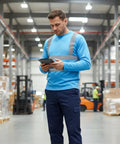 Heavy Duty Class Three High Visibility Long Sleeve Safety Shirt Loaded With Ansi Certified Reflective Tape Built Hella Tough For Your Daily Job Site Grind worn by a man checking a tablet in a warehouse.