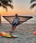 Ultralight Pocket Hammock For Solo Adventures set up between two palm trees on a beach at sunset, supports up to 330lbs.